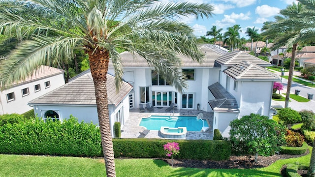 rear view of property with stucco siding, a tile roof, a pool with connected hot tub, and a patio