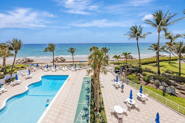 community pool featuring fence, view of water and beach, and a patio