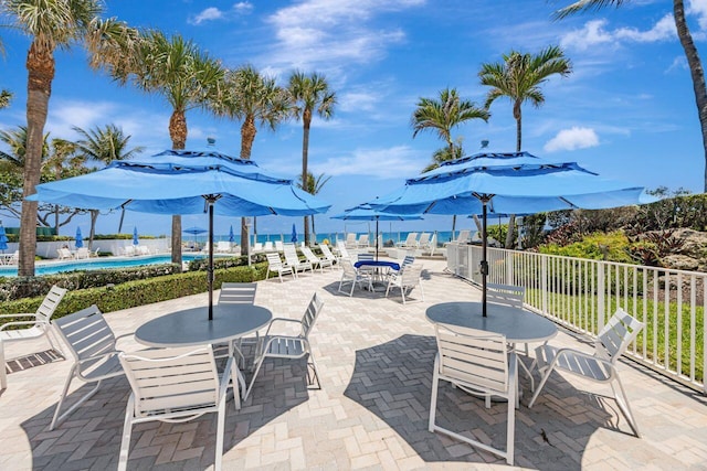 view of patio featuring a community pool, fence, and outdoor dining area