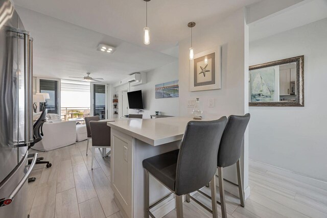 kitchen featuring high end fridge, a wall unit AC, a breakfast bar area, a ceiling fan, and light countertops