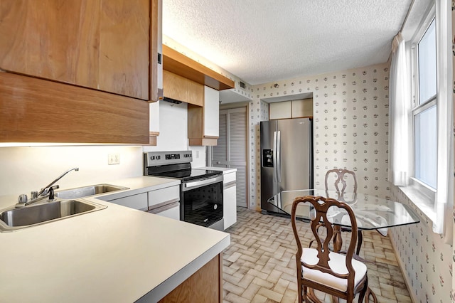 kitchen featuring appliances with stainless steel finishes, a sink, light countertops, a textured ceiling, and brick patterned flooring