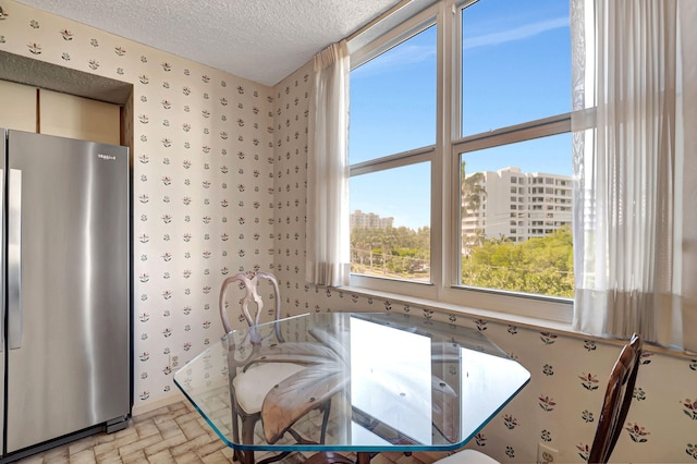 dining room featuring wallpapered walls, brick patterned flooring, a textured ceiling, and a city view