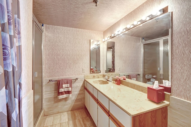 full bathroom featuring a shower stall, vanity, a textured ceiling, and wallpapered walls