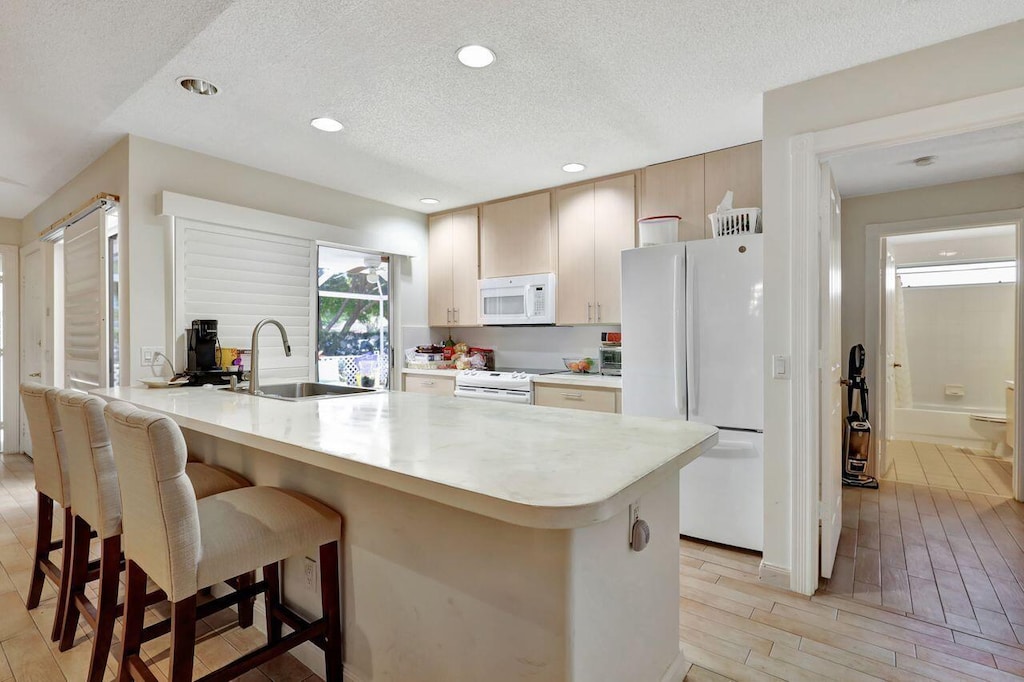 kitchen featuring white appliances, a sink, a kitchen bar, light countertops, and a peninsula