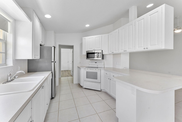 kitchen featuring appliances with stainless steel finishes, a sink, a peninsula, light countertops, and recessed lighting