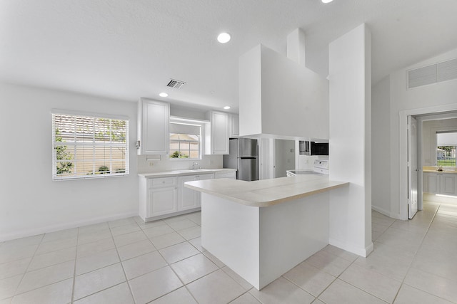kitchen with freestanding refrigerator, light countertops, range, a peninsula, and white cabinets