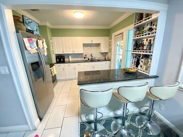 1119 S Ridge St, Lake Worth, FL 33460 - kitchen with stainless steel refrigerator with ice dispenser, white cabinetry, a sink, decorative backsplash, and crown molding