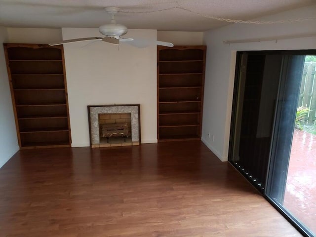unfurnished living room featuring wood finished floors, a ceiling fan, built in features, and a fireplace