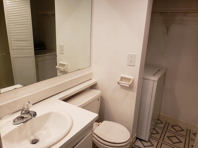 half bath with washer / clothes dryer, toilet, vanity, and baseboards