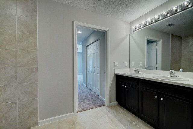 bathroom with double vanity, tile patterned floors, baseboards, and a textured ceiling