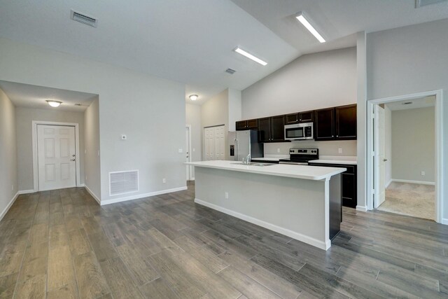 kitchen featuring appliances with stainless steel finishes, an island with sink, dark wood-type flooring, light countertops, and high vaulted ceiling
