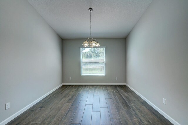 unfurnished room with a chandelier, dark wood finished floors, a textured ceiling, and baseboards
