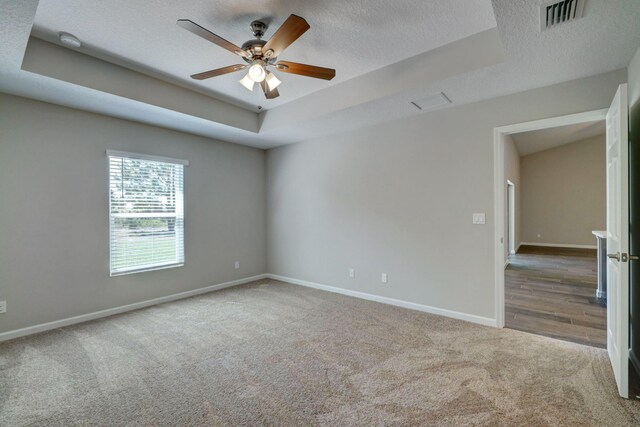 carpeted empty room featuring a tray ceiling, a textured ceiling, baseboards, a ceiling fan, and a smoke detector