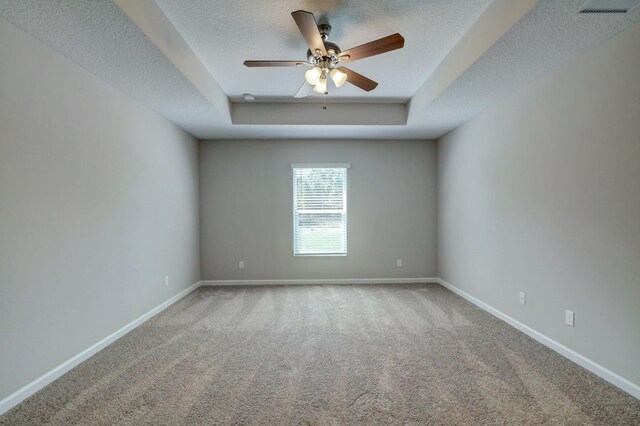 carpeted empty room with a raised ceiling, baseboards, ceiling fan, and a textured ceiling