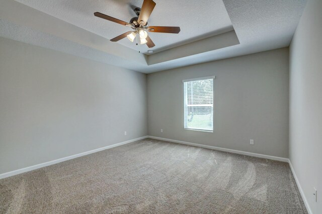 carpeted empty room with baseboards, a textured ceiling, ceiling fan, and a tray ceiling