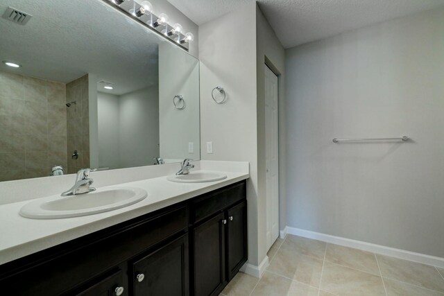 full bathroom featuring a tile shower, a textured ceiling, double vanity, tile patterned flooring, and baseboards