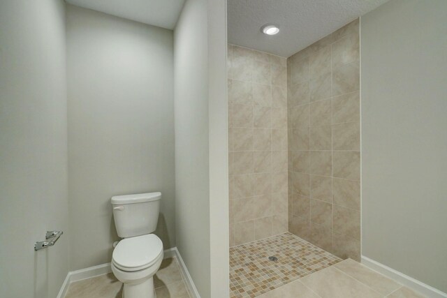 full bath with tile patterned flooring, a tile shower, toilet, baseboards, and a textured ceiling
