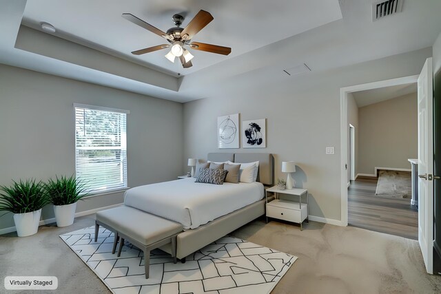bedroom featuring baseboards, light colored carpet, a raised ceiling, and ceiling fan