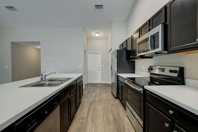kitchen featuring stainless steel appliances, a sink, light wood finished floors, and light countertops