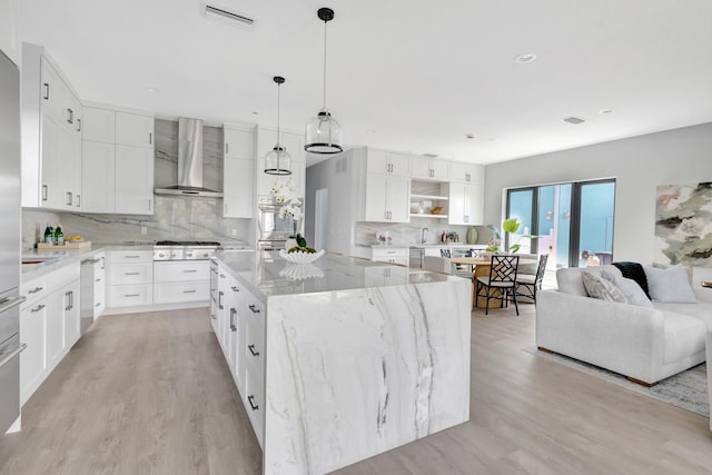 kitchen featuring wall chimney range hood, a kitchen island, tasteful backsplash, appliances with stainless steel finishes, and light wood finished floors