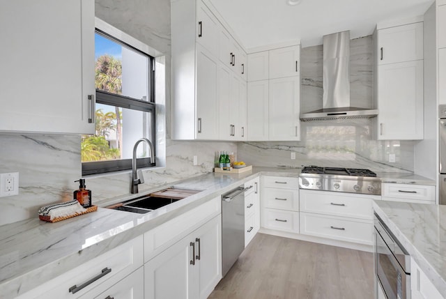 kitchen with wall chimney exhaust hood, a sink, appliances with stainless steel finishes, and white cabinetry