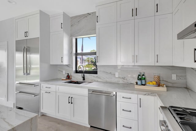 kitchen with appliances with stainless steel finishes, a sink, white cabinets, light stone counters, and backsplash