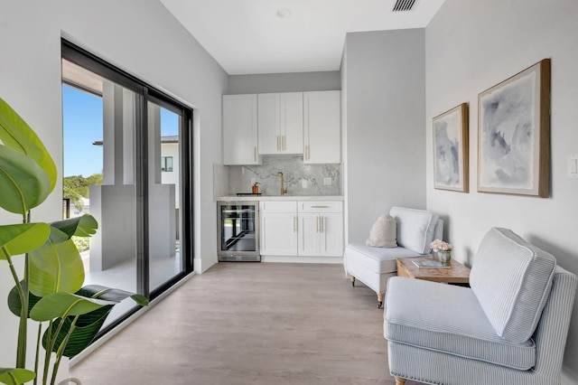 sitting room featuring wine cooler, light wood finished floors, and wet bar