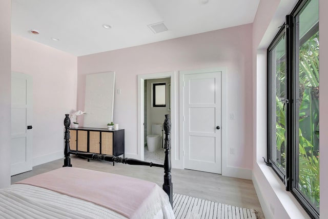 bedroom featuring multiple windows, light wood finished floors, baseboards, and connected bathroom