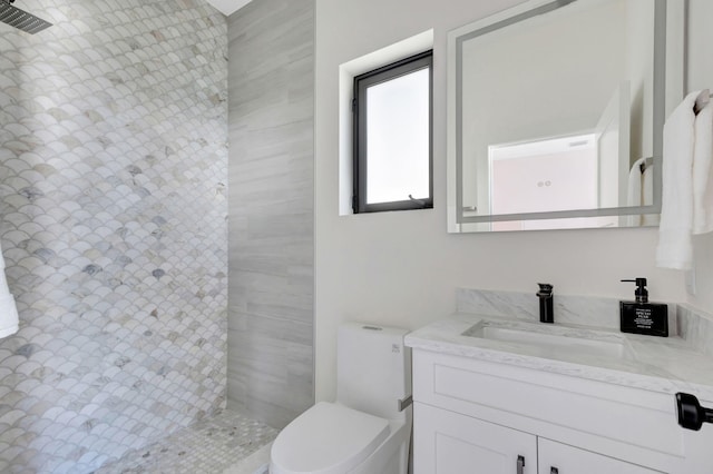 bathroom featuring a tile shower, toilet, and vanity