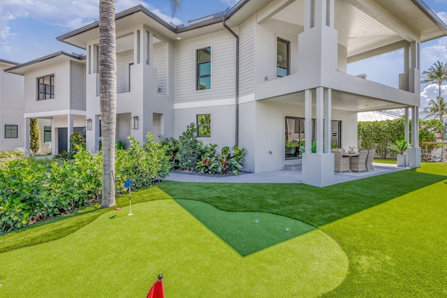rear view of house with an area to practice putting, a patio, stucco siding, and a balcony
