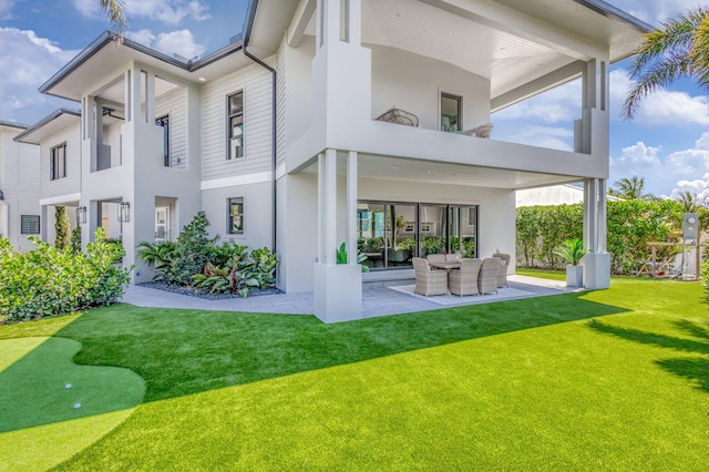 back of property featuring an area to practice putting, a balcony, stucco siding, a patio area, and a lawn