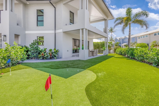 back of property with a putting area, a balcony, a patio area, and stucco siding
