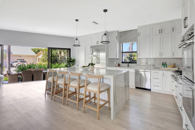 kitchen featuring stainless steel appliances, a sink, light wood-style floors, a breakfast bar area, and a center island
