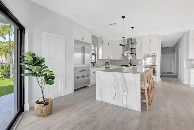 kitchen featuring appliances with stainless steel finishes, light wood-style flooring, wall chimney exhaust hood, a center island, and light stone counters