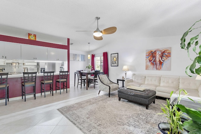 living area with ceiling fan, vaulted ceiling, light tile patterned flooring, and a textured ceiling