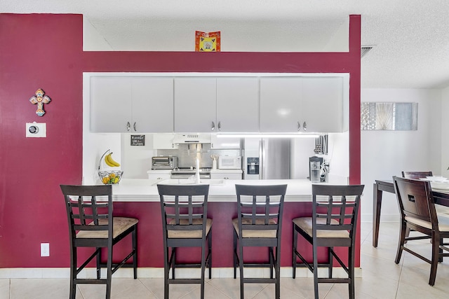 kitchen with stainless steel fridge, a peninsula, a textured ceiling, a kitchen breakfast bar, and under cabinet range hood