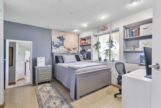 bedroom with a textured ceiling, light tile patterned flooring, and a desk
