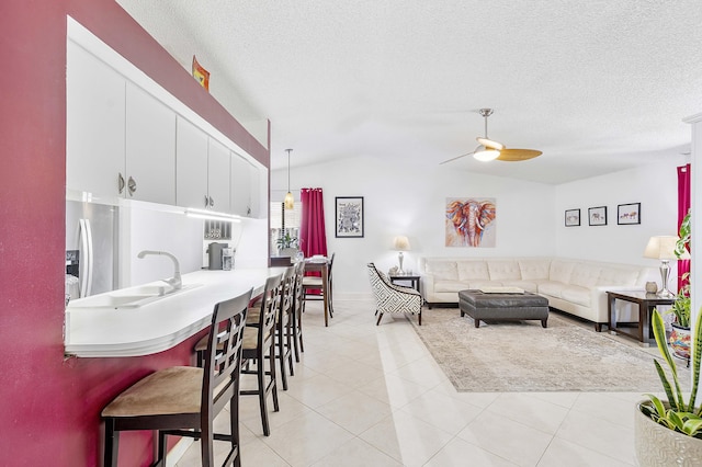living area featuring ceiling fan, vaulted ceiling, light tile patterned floors, a textured ceiling, and baseboards