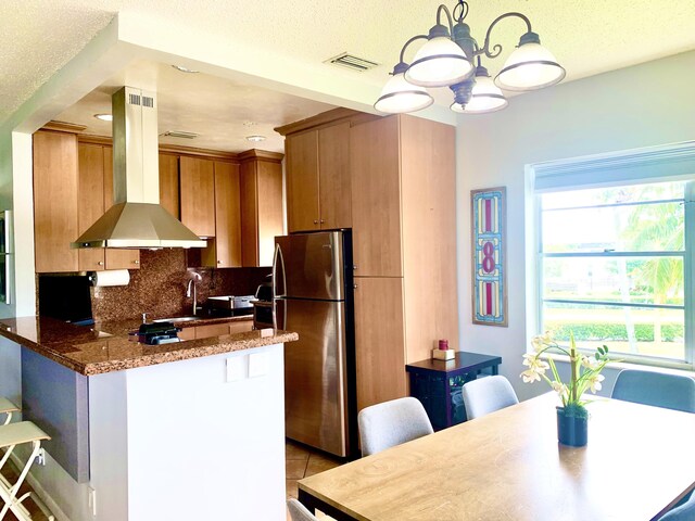 kitchen with freestanding refrigerator, island exhaust hood, a peninsula, backsplash, and a chandelier