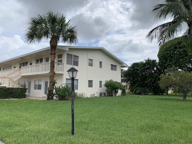 view of side of home featuring stucco siding, a lawn, central AC unit, and stairs