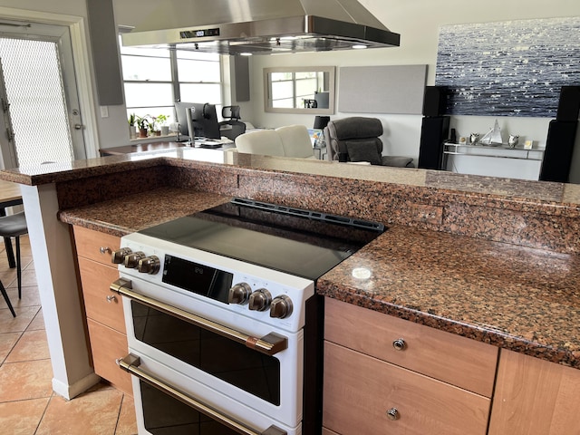 kitchen featuring double oven range, wall chimney range hood, light tile patterned floors, and open floor plan