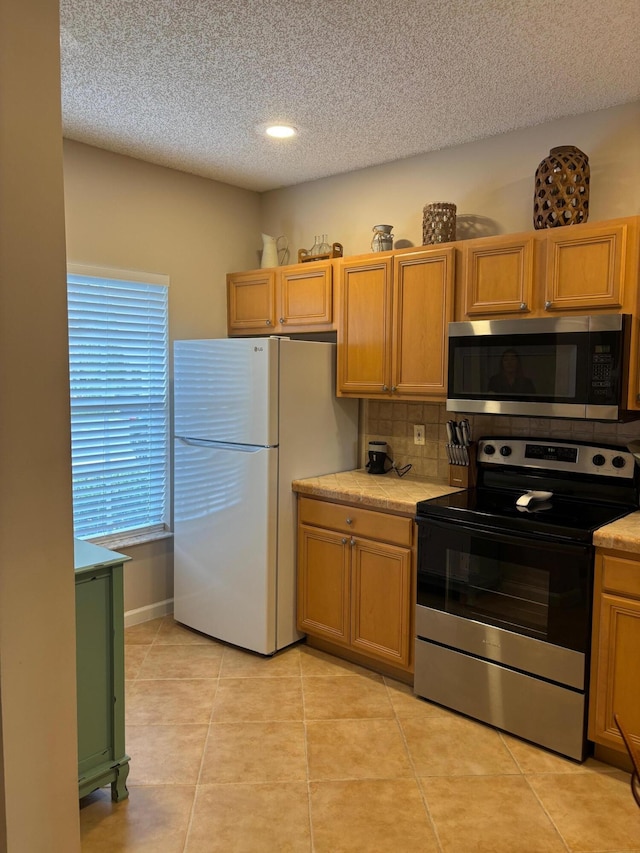 kitchen featuring stainless steel appliances, a textured ceiling, light countertops, light tile patterned floors, and tasteful backsplash
