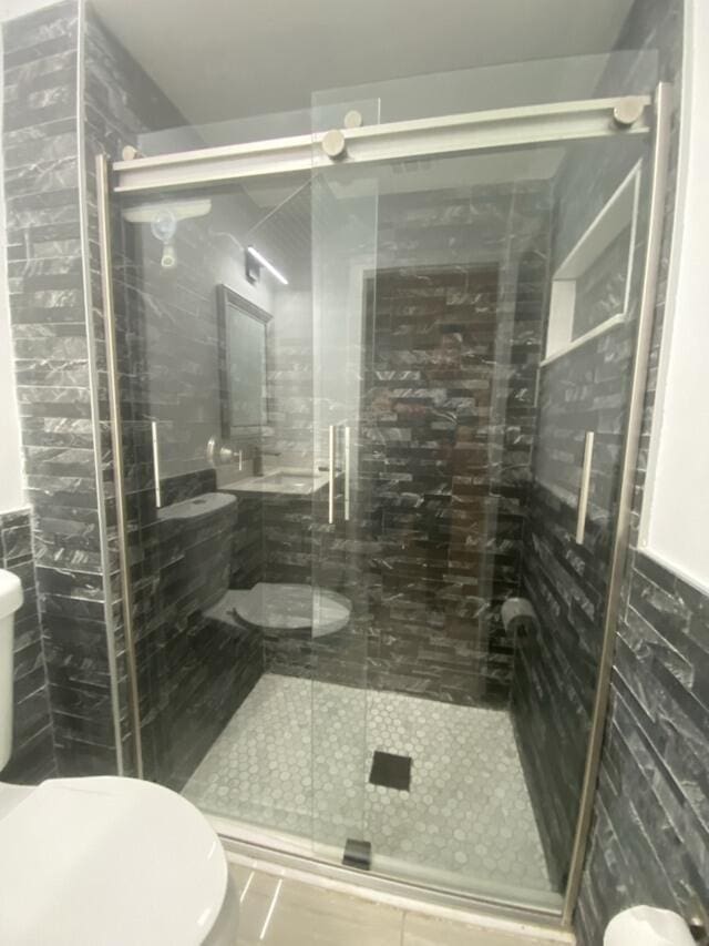 bathroom with toilet, tile walls, a shower stall, and wainscoting