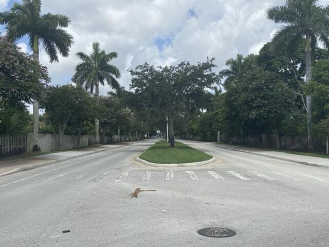 view of asphalt road with curbs, sidewalks, and view of wooded area