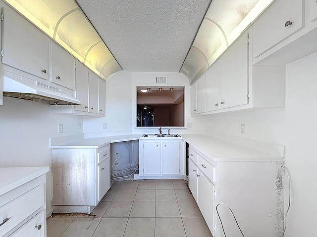 kitchen featuring a sink, under cabinet range hood, light countertops, light tile patterned floors, and a textured ceiling
