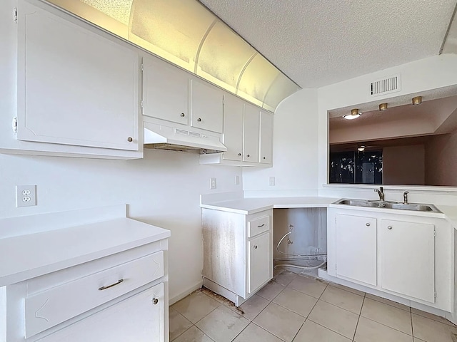 kitchen with under cabinet range hood, a sink, light tile patterned floors, light countertops, and a textured ceiling