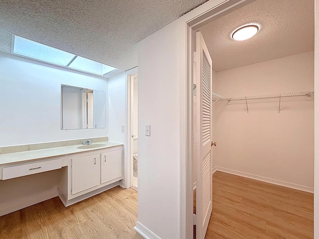 bathroom with a textured ceiling, wood finished floors, vanity, a skylight, and a spacious closet