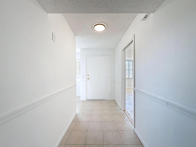 hallway with a textured ceiling and light tile patterned flooring