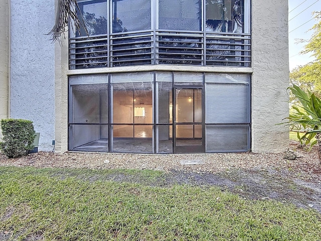rear view of property with a balcony, stucco siding, and a yard