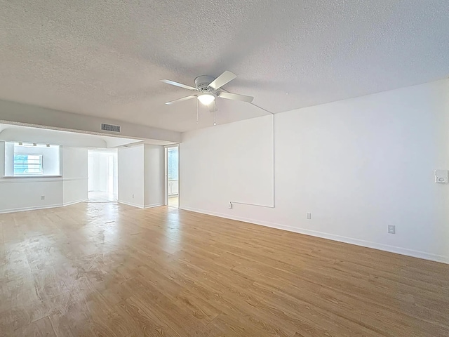 empty room with a ceiling fan, a textured ceiling, light wood-type flooring, and baseboards